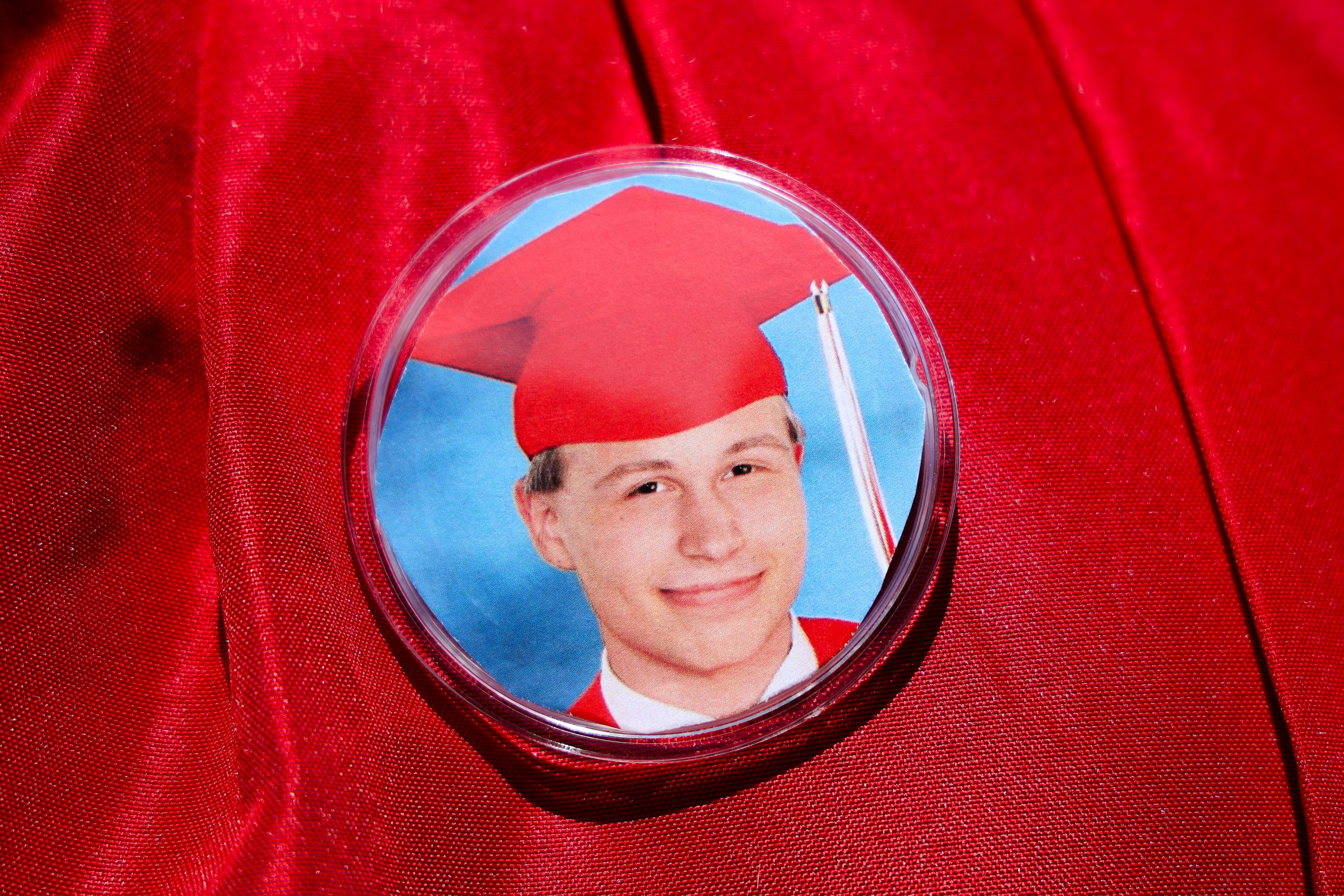 A close up of a red gown with a pin bearing a photo of a student in a red cap and gown