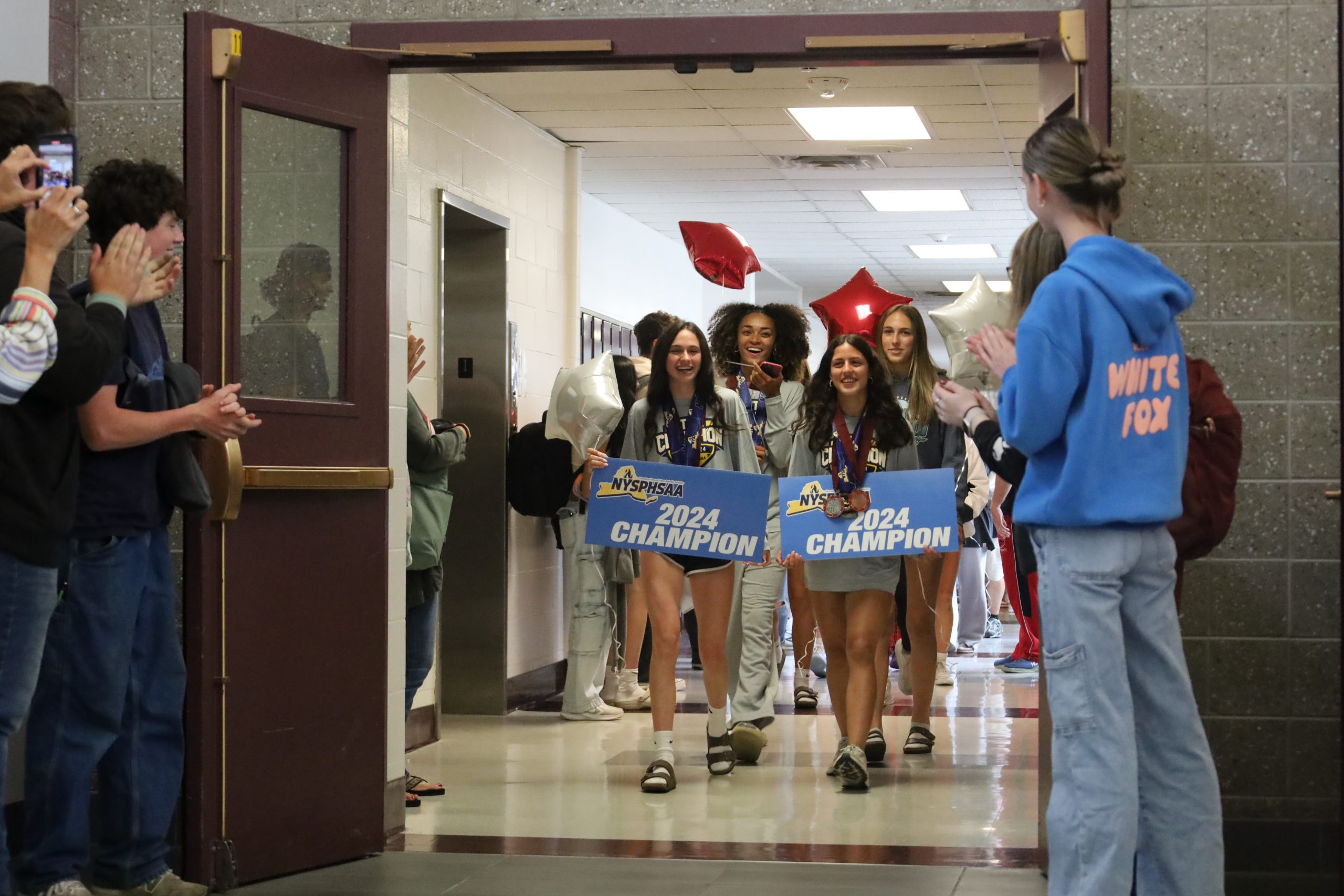 Track and field athletes walk the halls of GHS holding signs and balloons. Students are lining the halls, applauding