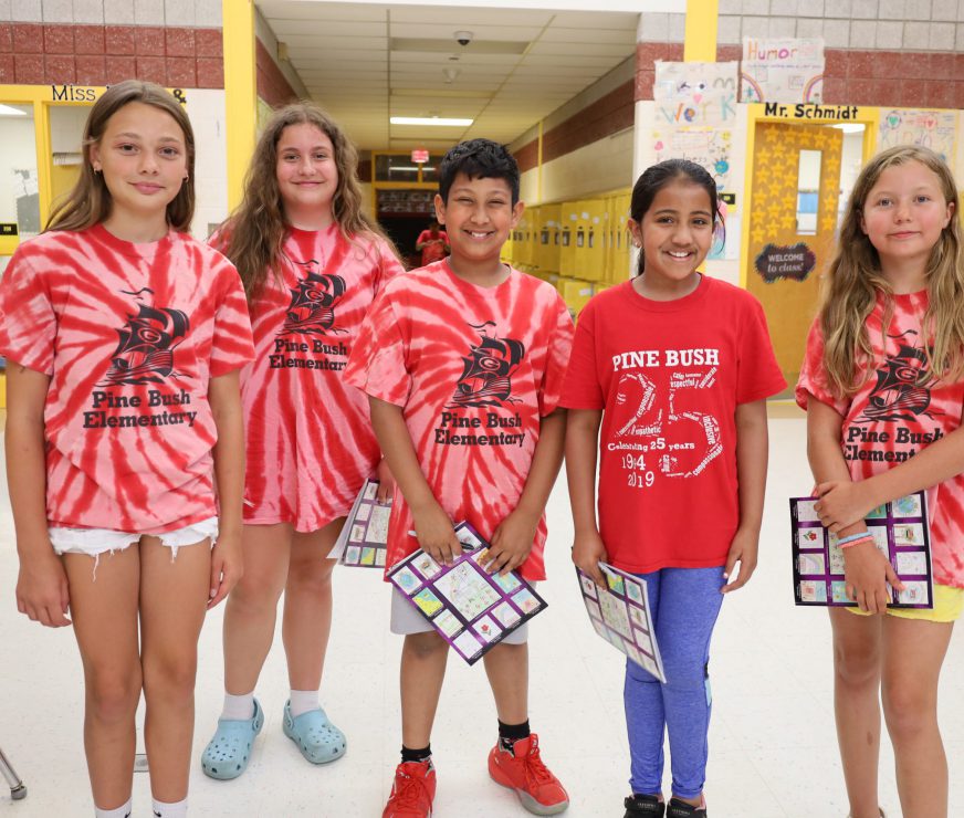 Five Pine Bush Elementary students standing in a line smiling with their school pride shirts on.