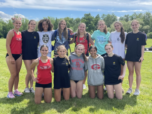 The GHS girls track and field team poses together outside. They are in two rows. Some are kneeling and some are standing. They have their arms around each other