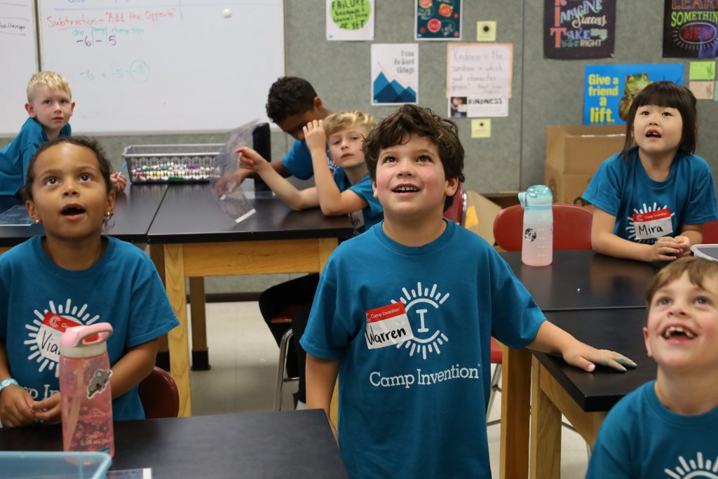 Elementary students looking up at the ceiling and smiling.