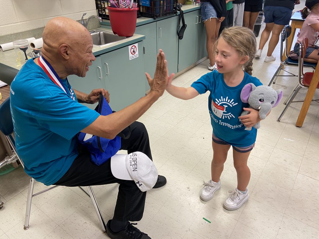 Man is high fiving an elementary student, who's holding a stuffed elephant in her right hand.