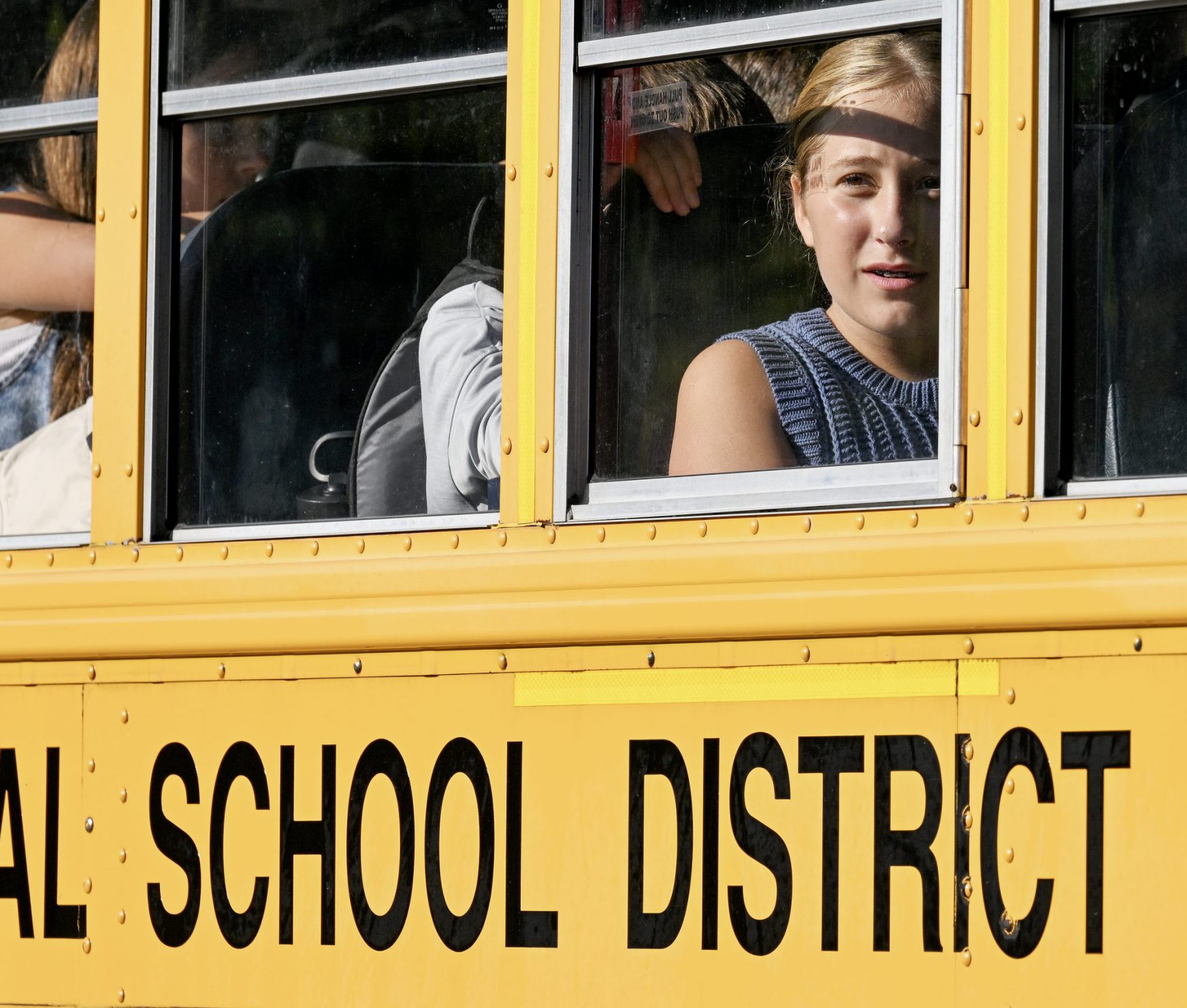 Students on the bus on the first day of school. One student is looking out of the window.