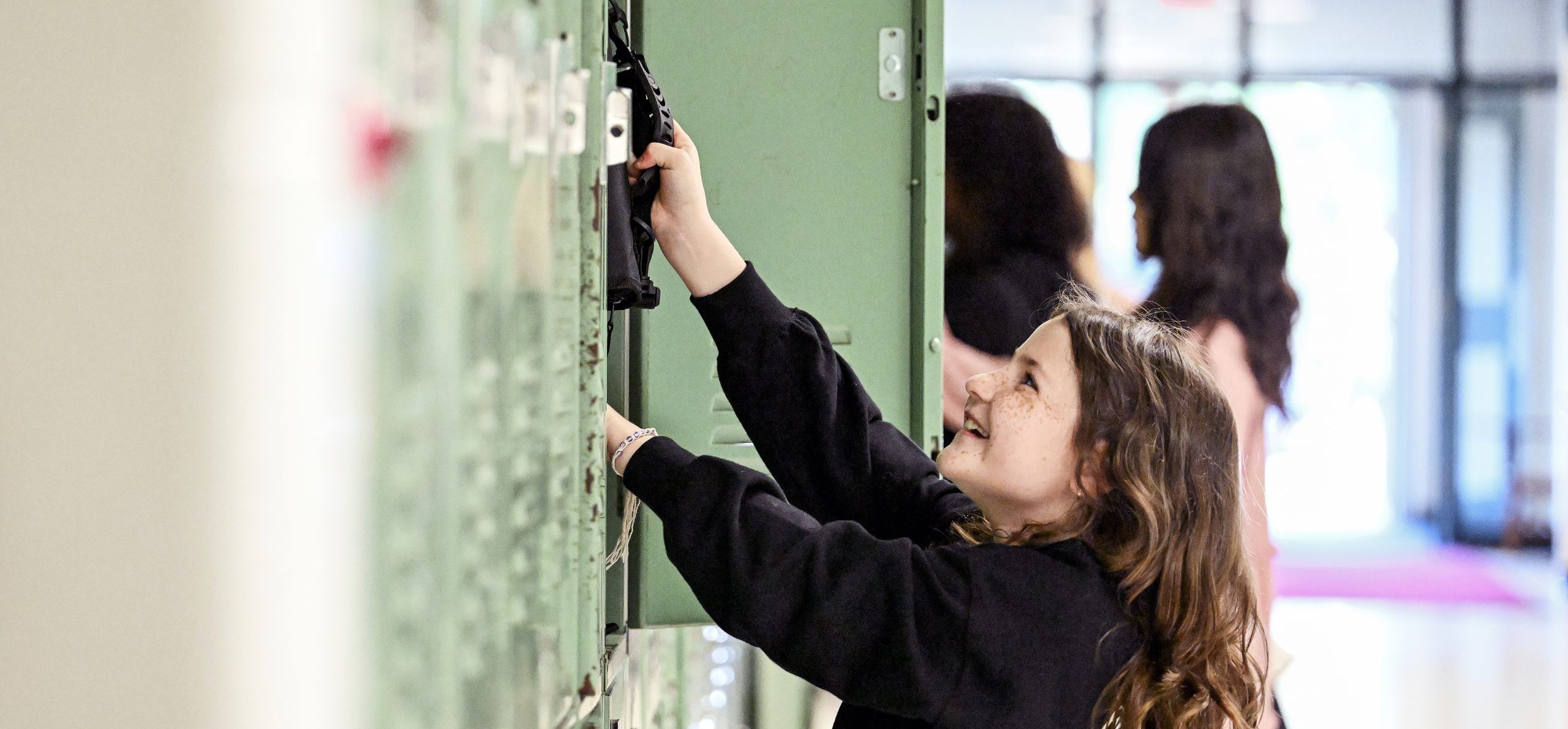 Middle school student smiling and grabbing something from her locker.