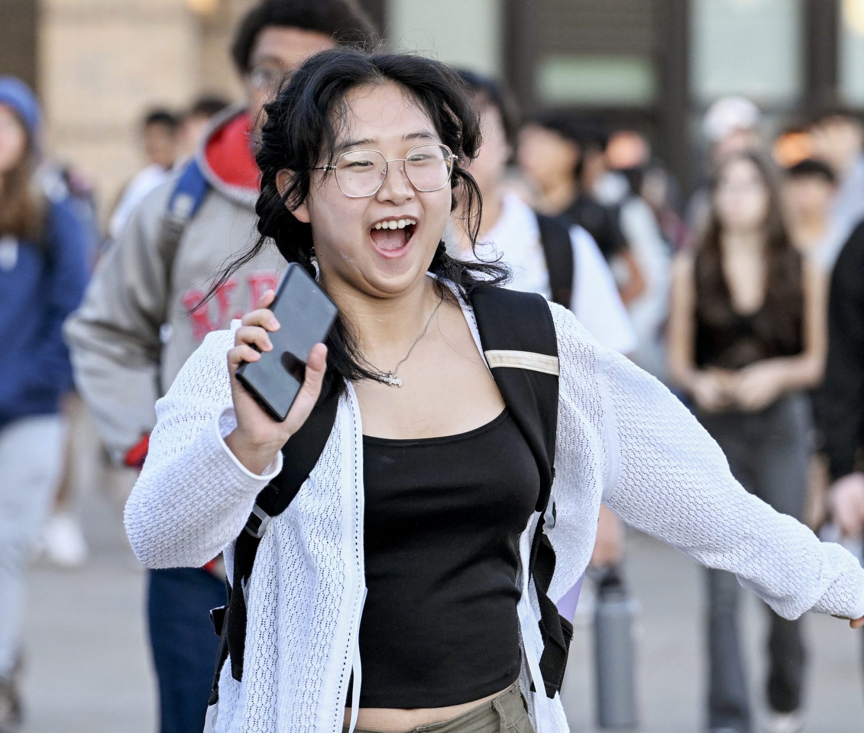 Student running to a friend on the first day of school. She is outside of the school and smiling.