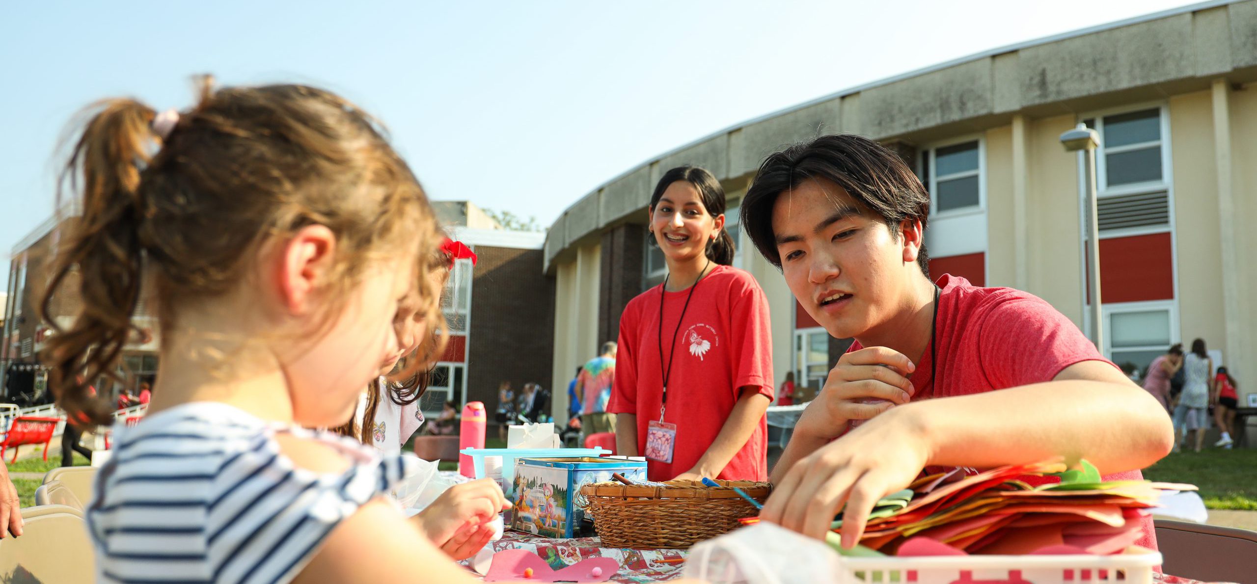 Two middle school students helping a child with crafts at the 25th Butterfly Station Anniversary. The middle school students are smiling. They are outside of the school.