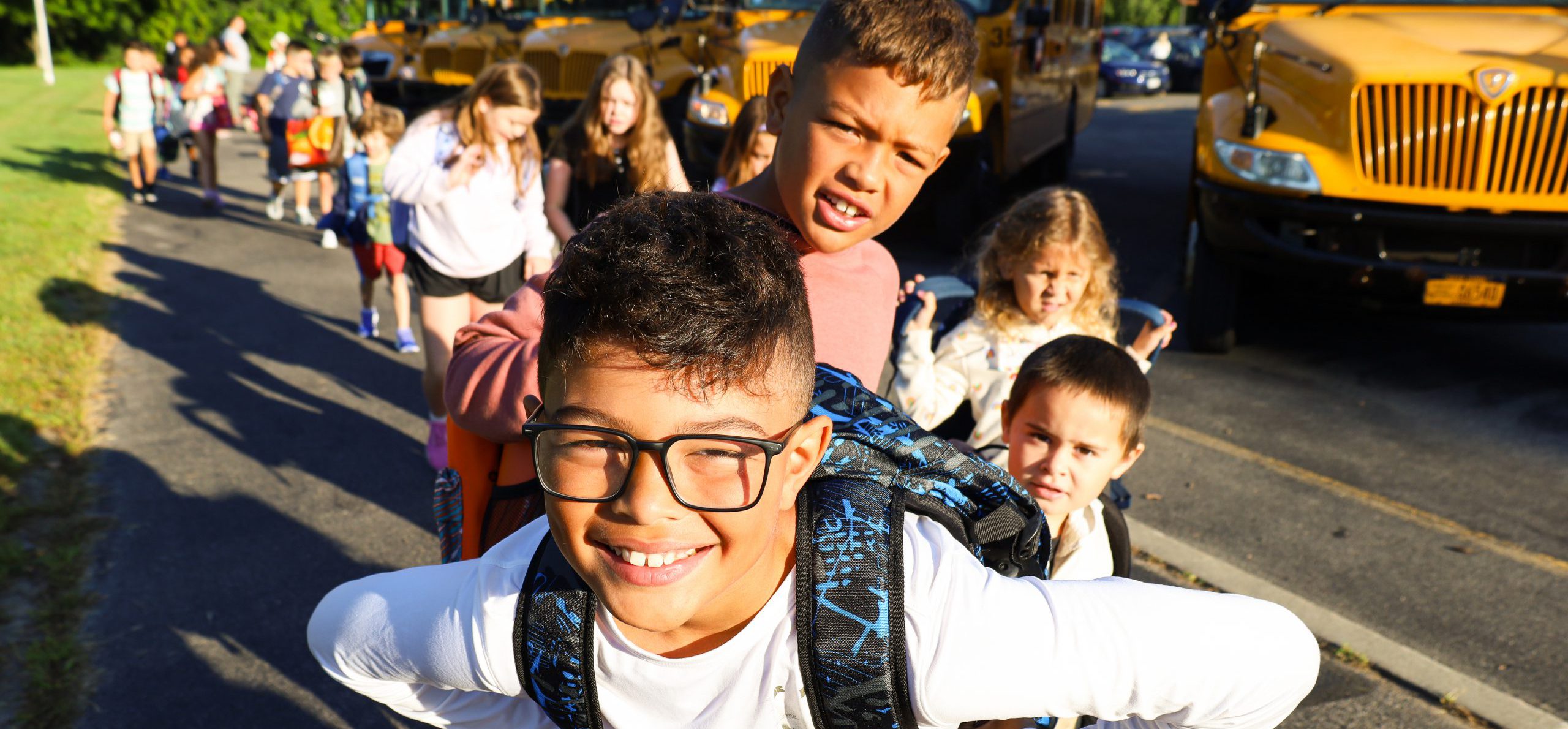 Elementary school students smiling in front of the bus. It is the first day of school.