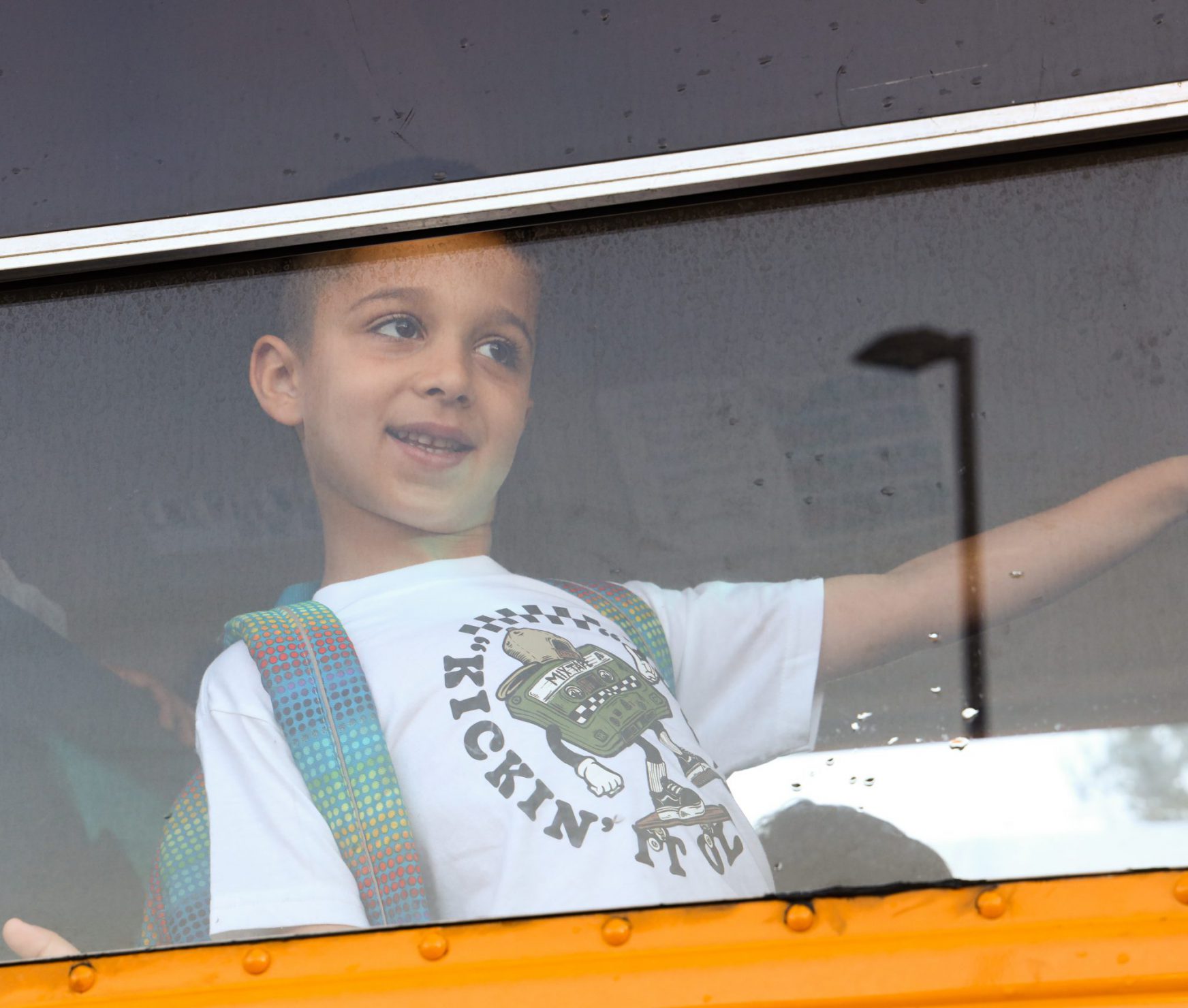 Student with backpack on. He is sitting on a school bus smiling.