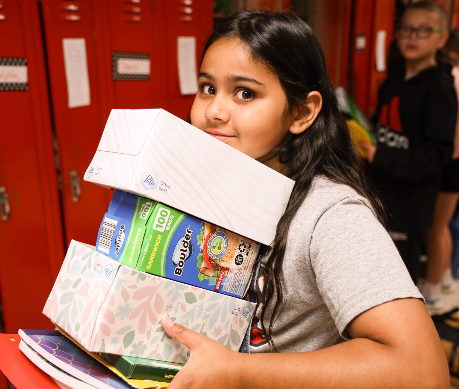 Student smiling while holding supplies. She is walking into her class on the first day of school.