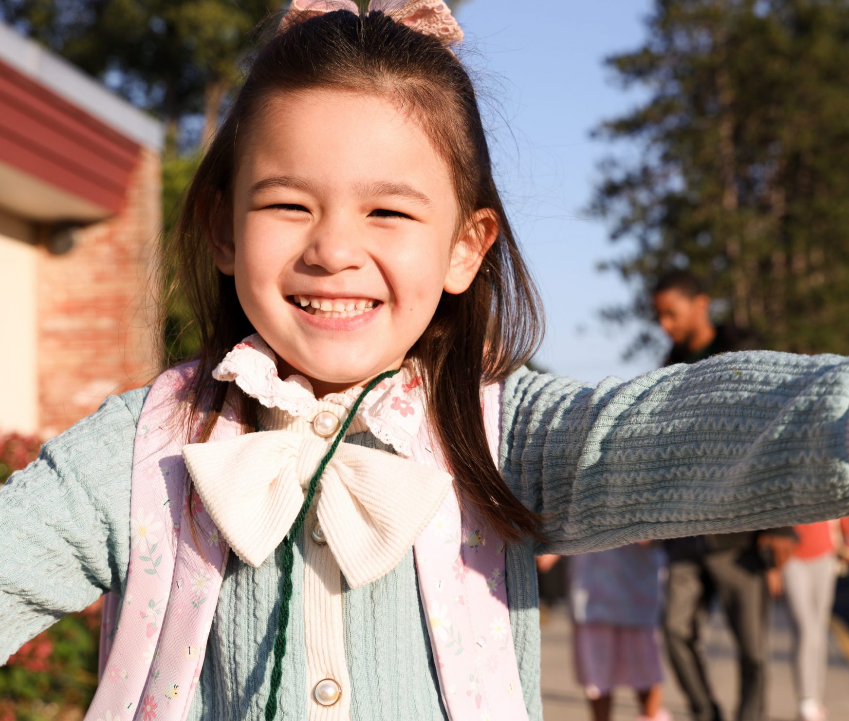 Student smiling on the first day of school. She is standing in front of the school.