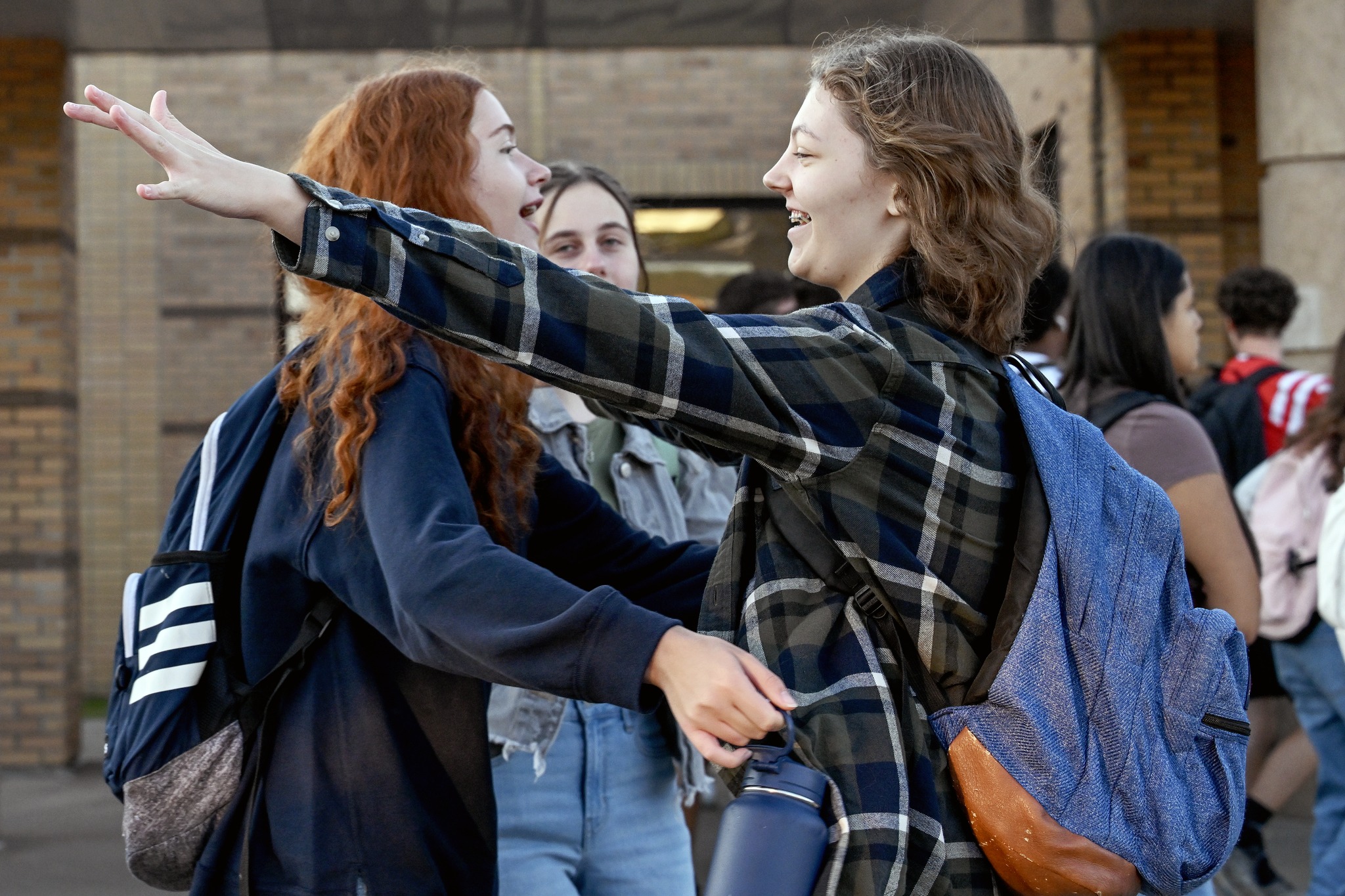 Two students greet each other in front of the high school. They are smiling and getting ready to hug each other