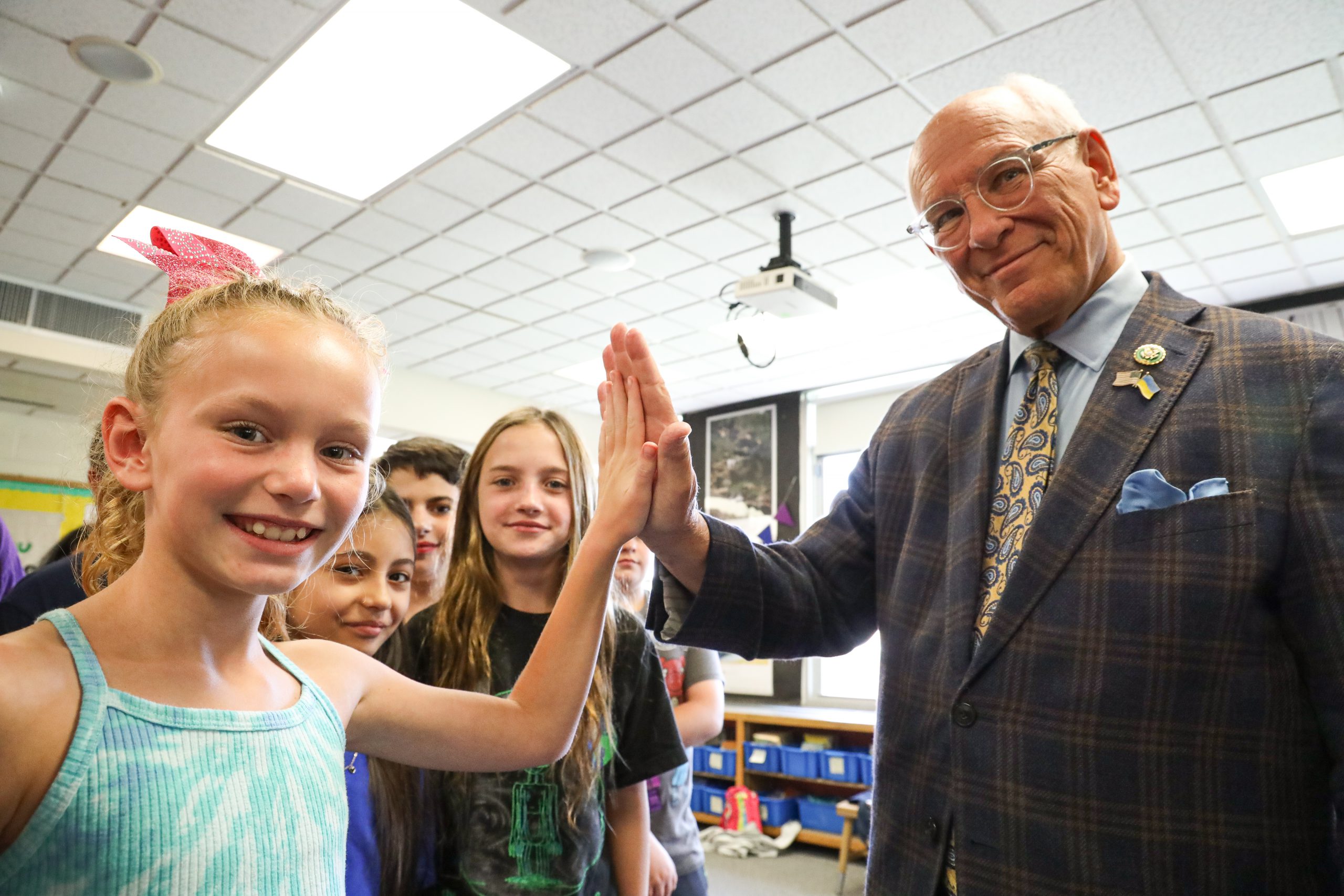 A man wearing a sport coat, shirt and tie high fives a student who is wearing a turquoise blue tie-dyed shirt. The are both smiling at the camera