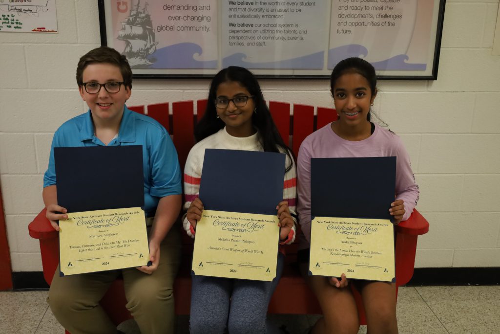 Three Farnsworth Middle School students sitting together with their achievement awards.