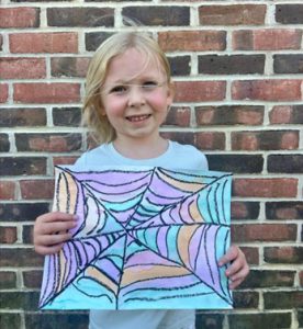 Elementary student holding artwork and smiling. 