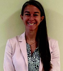 Christine Cochrane is wearing a pink jacket with a black and white patterned shirt under the jacket. She is smiling at the camera