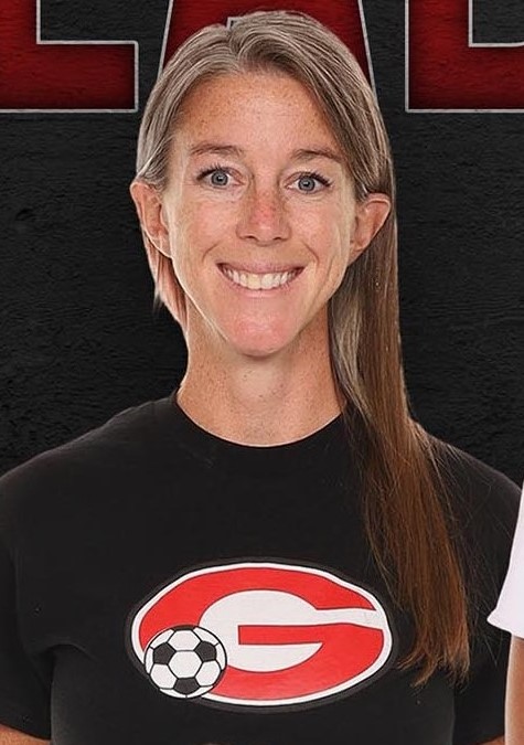 Christine Cochrane is smiling at the camera, her hair is over one shoulder. She is wearing a black t-shirt with a red G and a small soccer ball on the front of the t-shirt