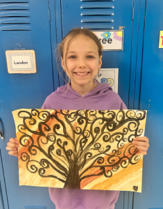 Elementary student holding artwork and smiling.