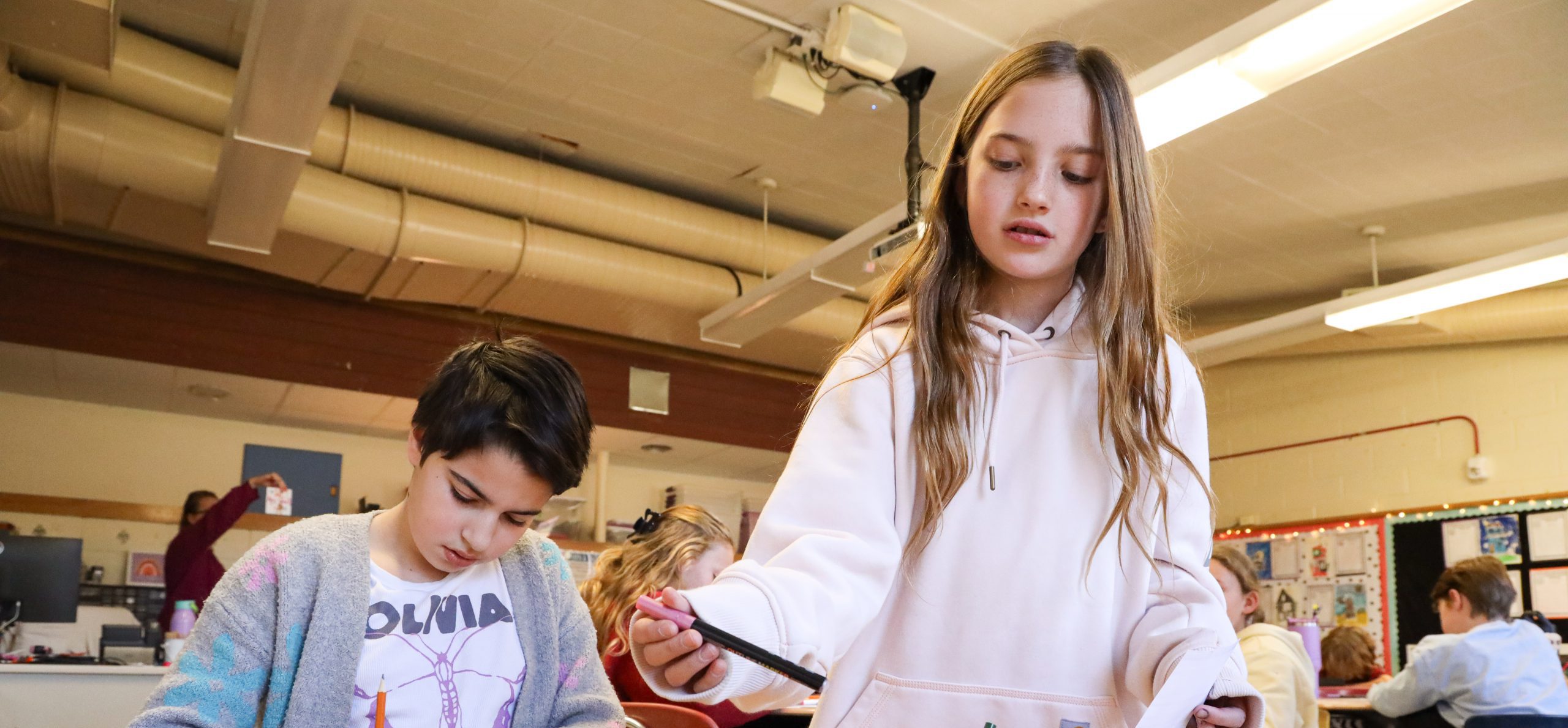 Two students creating art and one is reaching for a marker.