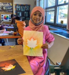 Elementary student holding artwork and smiling.