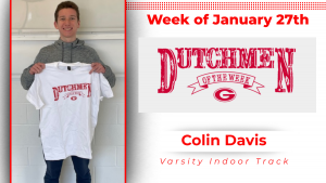 A student stands in front of a white wall holding a white t-shirt with red type that reads Dutchmen of the Week