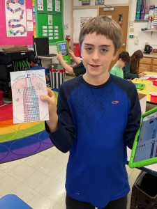 Elementary student holding artwork and smiling.