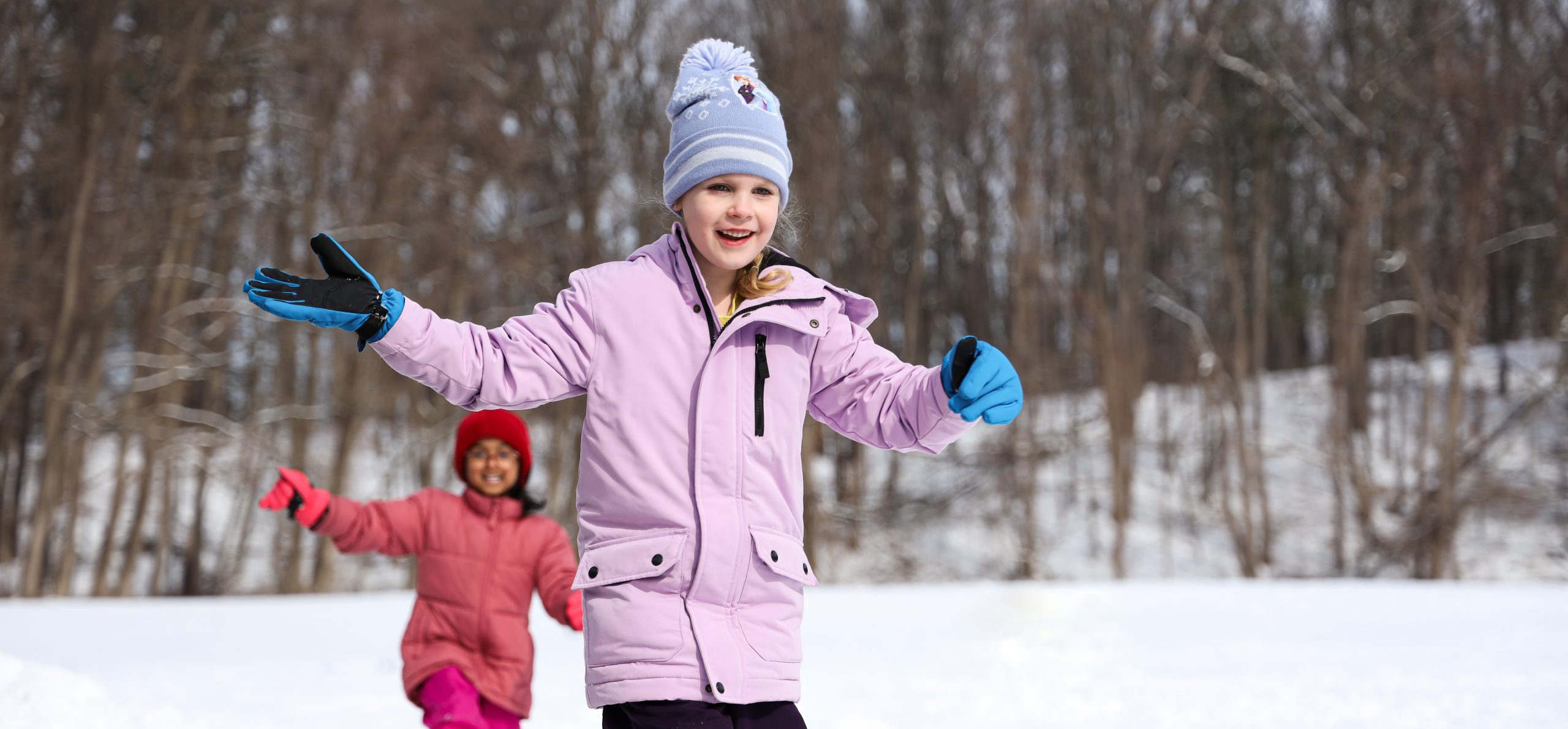 Students playing outside in the snow during recess. One student is smiling and running.