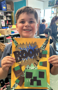 Elementary student holding artwork and smiling.