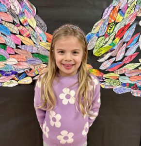 Elementary student holding artwork and smiling.