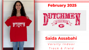 A student stands in front of a white wall, holding a red t-shirt with white lettering that reads "Dutchmen of the Week."