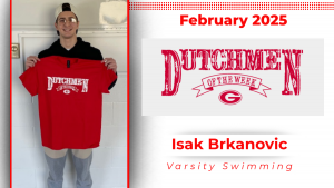 A student stands in front of a white wall, holding a red t-shirt with white lettering that reads "Dutchmen of the Week."