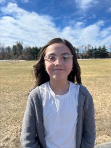 A student is standing in outside, smiling. The sky is blue with puffy white clouds