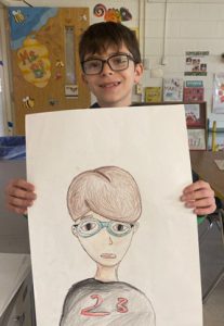 A student is standing in a classroom, holding a piece of artwork